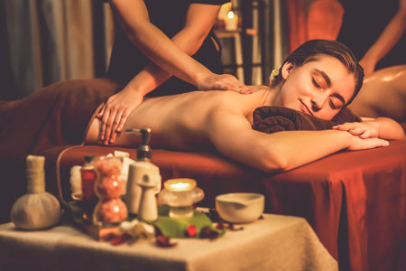 Caucasian couple customer enjoying relaxing anti-stress spa massage and pampering with beauty skin recreation leisure in warm candle lighting ambient salon spa at luxury resort or hotel. Quiescentの写真素材