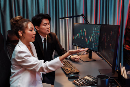 Smiling Asian business traders pointing to dynamic stock exchange data screen profit value online...