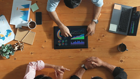Top aerial view of business man present financial graph to group of smart investors. Professional male leader analyze graph and explain marketing idea by using tablet on meeting table. Convocation.の写真素材