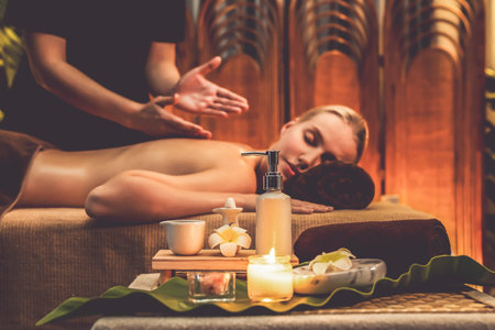 Aromatherapy massage ambiance or spa salon composition setup with focus decor candles and spa accessories on blurred woman enjoying blissful aroma spa massage in resort or hotel background. Quiescentの写真素材