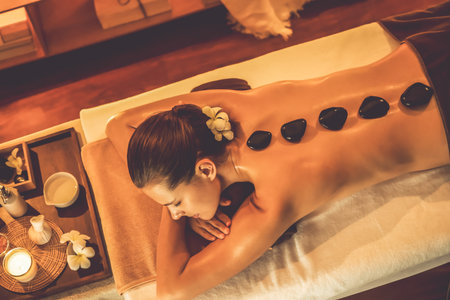 Hot stone massage at spa salon in luxury resort with warm candle light, blissful woman customer enjoying spa basalt stone massage glide over body with soothing warmth. Quiescentの写真素材