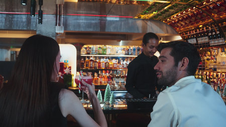 Bartender serving mixed punch cocktail Christmas theme garnished with candy cane serving to woman...