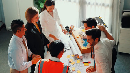 Top view of skilled architect engineer team inspect house model while project manager hold blueprint and asking about building construction. Group of diverse engineers working together.の写真素材