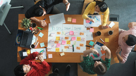Top down aerial view of smart business team making scrum task board at meeting room. Group of smart people writing at paper and sticky notes for making kanban board and giving high five. Convocation.の写真素材
