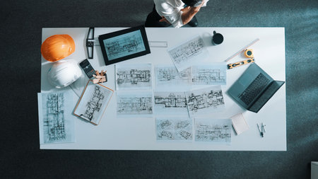 Top down view of engineer looking at tablet while using laptop to analysis building structure. Aerial view of architect checking at interior design at meeting table with project plan.の写真素材