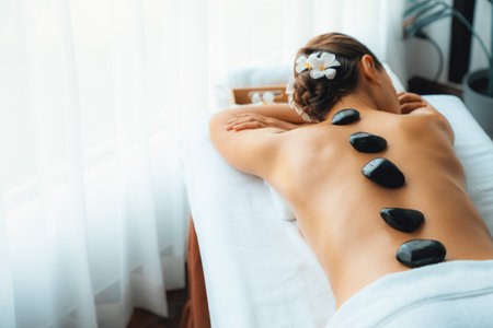 Hot stone massage at spa salon in luxury resort with day light serenity ambient, blissful woman customer enjoying spa basalt stone massage glide over body with soothing warmth. Quiescentの写真素材