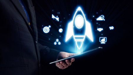 A businessman displays a tablet showcasing a holographic rocket symbolizing growth and innovation amid digital icons representing business success and technology in a dark space. Qubitの写真素材
