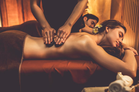 Hot stone massage at spa salon in luxury resort with warm candle light, blissful couple customer enjoying spa basalt stone massage glide over body with soothing warmth. Quiescentの写真素材