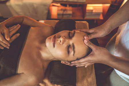 Caucasian woman enjoying relaxing anti-stress head massage and pampering facial beauty skin recreation leisure in warm candle lighting ambient salon spa in luxury resort or hotel. Quiescentの写真素材