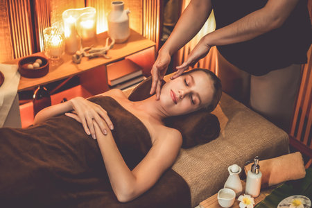 Caucasian woman enjoying relaxing anti-stress head massage and pampering facial beauty skin recreation leisure in warm candle lighting ambient salon spa in luxury resort or hotel. Quiescentの写真素材
