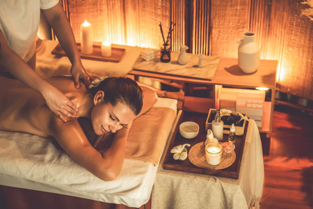 Caucasian woman customer enjoying relaxing anti-stress spa massage and pampering with beauty skin recreation leisure in warm candle lighting ambient salon spa at luxury resort or hotel. Quiescentの写真素材