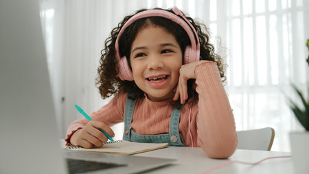 Side view of smart girl take off headphone and doing homework in self study. Caucasian schoolgirl writing at notebook while searching about programing system and writing engineering prompt. Pedagogy.の写真素材