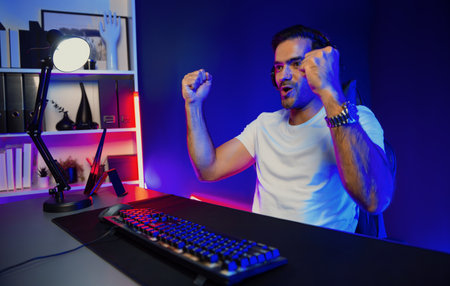 Winner of smart streamer playing online game wearing headphones raising fist up on streaming gamer with social media. Esport skill team player online digital gaming at neon light studio room. Surmise.の写真素材