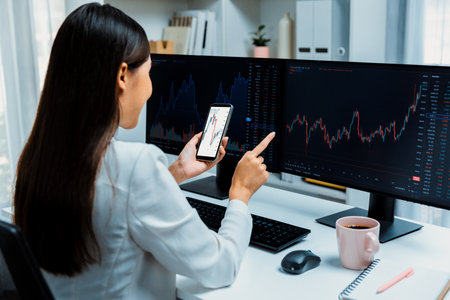 Smiling young Asian businesswoman with happy face looking on smartphone in profitable of exchange stock market graph at modern office. Concept of investing high profit in wealth security. Stratagem.の写真素材
