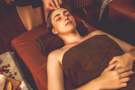 Caucasian woman enjoying relaxing anti-stress head massage and pampering facial beauty skin recreation leisure in warm candle lighting ambient salon spa in luxury resort or hotel. Quiescentの写真素材