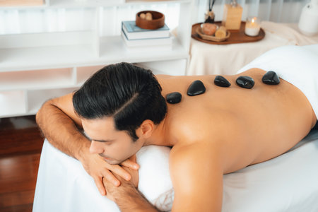 Hot stone massage at spa salon in luxury resort with day light serenity ambient, blissful man customer enjoying spa basalt stone massage glide over body with soothing warmth. Quiescentの写真素材