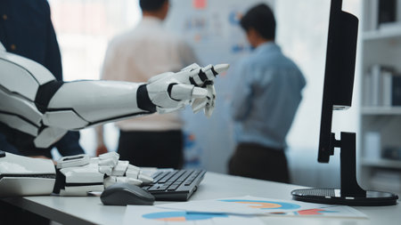 A robotic hand gestures over a keyboard, illustrating the blend of technology and human interaction in a contemporary office environment focused on productivity and innovation.の写真素材