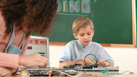 Caucasian smart boy fixing main board by using screwdriver at stem technology lesson while smiling student working together to inspect electronic machine at table with laptop display code. Pedagogy.の写真素材