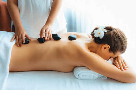 Hot stone massage at spa salon in luxury resort with day light serenity ambient, blissful woman customer enjoying spa basalt stone massage glide over body with soothing warmth. Quiescentの写真素材