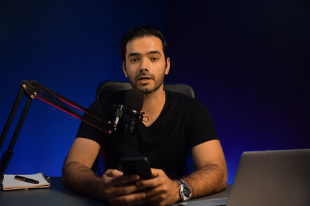 Broadcaster talking to listener on live streaming online, checking message from smartphone on social media in host channel by creative positive thinking concept at purple neon light studio. Surmise.の写真素材