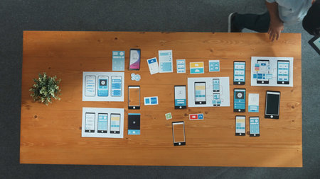 Top down view of software developer holding tablet while choosing icon for mobile phone interface or...