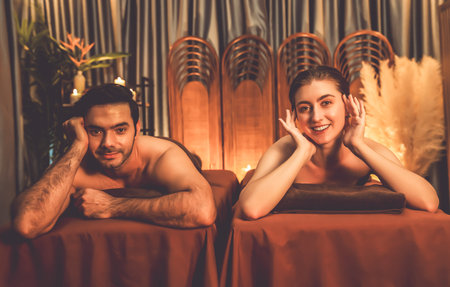 Caucasian couple customer enjoying relaxing anti-stress spa massage and pampering with beauty skin recreation leisure in warm candle lighting ambient salon spa at luxury resort or hotel. Quiescentの写真素材