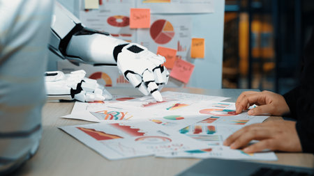 A human and robot work together in a modern office, analyzing various charts and graphs,...
