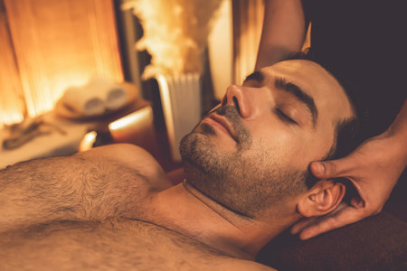 Caucasian man enjoying relaxing anti-stress head massage and pampering facial beauty skin recreation leisure in warm candle lighting ambient salon spa in luxury resort or hotel. Quiescentの写真素材