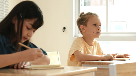 Smart student answer teachers question while sitting at classroom. Diverse children learning and studying while looking at blackboard and attend in elementary classroom. Education concept. Pedagogy.の写真素材