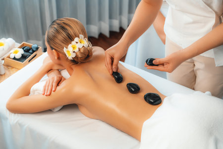 Hot stone massage at spa salon in luxury resort with day light serenity ambient, blissful woman customer enjoying spa basalt stone massage glide over body with soothing warmth. Quiescentの写真素材