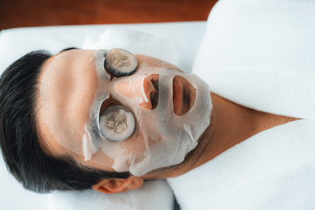 Serene daylight ambiance of spa salon, man customer indulges in rejuvenating with luxurious cucumber facial mask. Facial skincare treatment and beauty care concept. Quiescentの写真素材