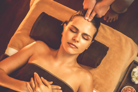Caucasian woman enjoying relaxing anti-stress head massage and pampering facial beauty skin recreation leisure in warm candle lighting ambient salon spa in luxury resort or hotel. Quiescentの写真素材