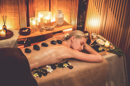 Hot stone massage at spa salon in luxury resort with warm candle light, blissful woman customer enjoying spa basalt stone massage glide over body with soothing warmth. Quiescentの写真素材