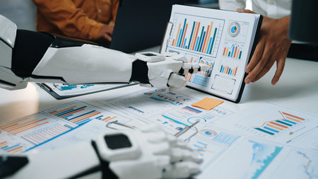 A futuristic robot assistant is engaging in data analysis, showcasing various charts and graphs in a modern office setting, highlighting technology advancements in teamwork.の写真素材