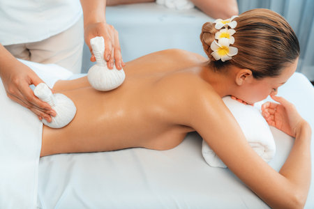 Hot herbal ball spa massage body treatment, masseur gently compresses herb bag on couple customer body. Tranquil and serenity of aromatherapy recreation in day lighting ambient at spa salon. Quiescentの写真素材
