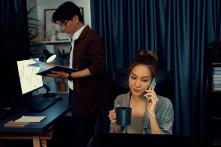 Businesswoman calling with customers with drinking coffee to make new project job at modern office while coworker checking paperwork business plan database report meeting at over late night. Infobahn.の写真素材