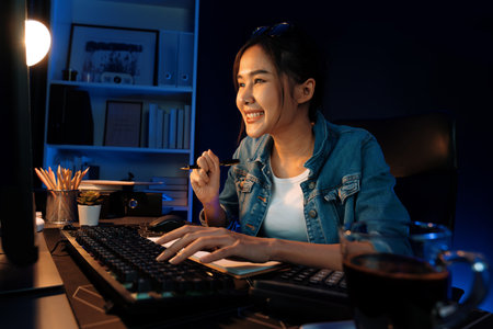 Smiling young beautiful asian creative officer looking on pc in sales target online, earning jobs freelancer for planning invest new strategy marketing online planning at neon light night. Stratagem.の写真素材