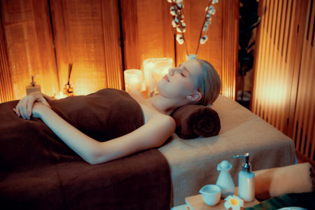 Caucasian woman customer enjoying relaxing anti-stress spa massage and pampering with beauty skin recreation leisure in warm candle lighting ambient salon spa at luxury resort or hotel. Quiescentの写真素材