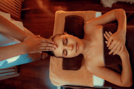 Caucasian woman enjoying relaxing anti-stress head massage and pampering facial beauty skin recreation leisure in warm candle lighting ambient salon spa in luxury resort or hotel. Quiescentの写真素材