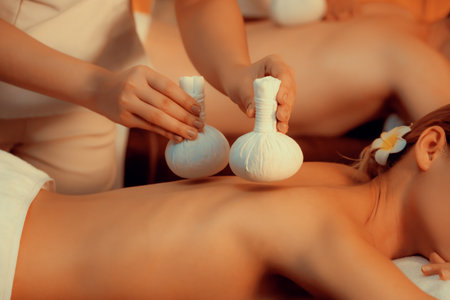 Closeup hot herbal ball spa massage body treatment, masseur gently compresses herb bag on couple customer body. Serenity of aromatherapy recreation in warm lighting of candles at spa salon. Quiescentの写真素材