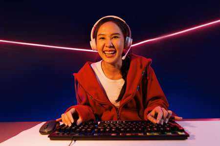 Host channel of smiling beautiful Asian girl streamer playing online game wearing headphone talking with viewers media online recording phone. Esport skilled team players in neon blue room. Stratagem.の写真素材