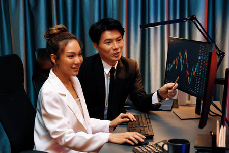 Smiling Asian business traders pointing to dynamic stock exchange data screen profit value online...