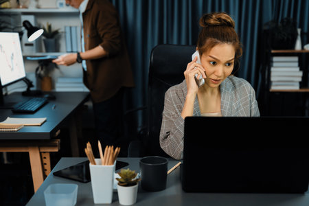 Businesswoman calling with customers to make new project job at modern office while coworker checking paperwork folder of business plan to database report meeting at over late night time. Infobahn.の写真素材