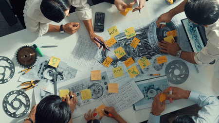 Top view of smart engineer team in casual cloth talking about turbine engine structure at table with metal gear, calculator, sticky notes. Group of technician taking a note in meeting.の写真素材