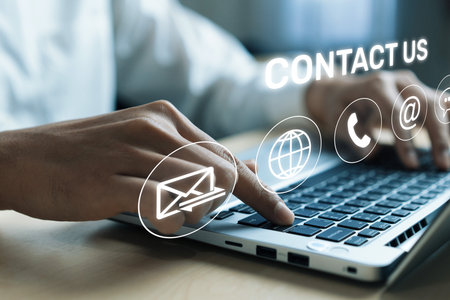 A close-up of hands on a laptop keyboard with digital Contact Us icons, symbolizing online customer...