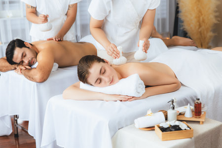 Hot herbal ball spa massage body treatment, masseur gently compresses herb bag on couple customer body. Tranquil and serenity of aromatherapy recreation in day lighting ambient at spa salon. Quiescentの写真素材