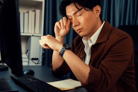 Working businessman feeling extremely tired with sleepy while working on desk with unfinish project at workplace, planing online business using information project at over late night time. Infobahn.の写真素材