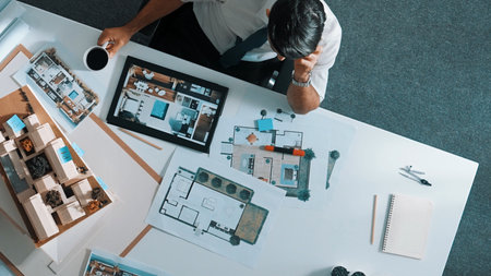 Top view of engineer drink coffee and thinking about house plan at meeting table with equipment and safety helmet scatter around. Aerial view of stressful manager looking at blueprint. Alimentation.の写真素材