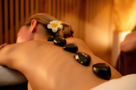 Hot stone massage at spa salon in luxury resort with warm candle light, blissful woman customer enjoying spa basalt stone massage glide over body with soothing warmth. Quiescentの写真素材