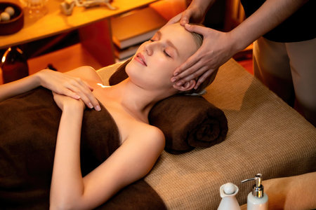 Caucasian woman enjoying relaxing anti-stress head massage and pampering facial beauty skin recreation leisure in warm candle lighting ambient salon spa in luxury resort or hotel. Quiescentの写真素材